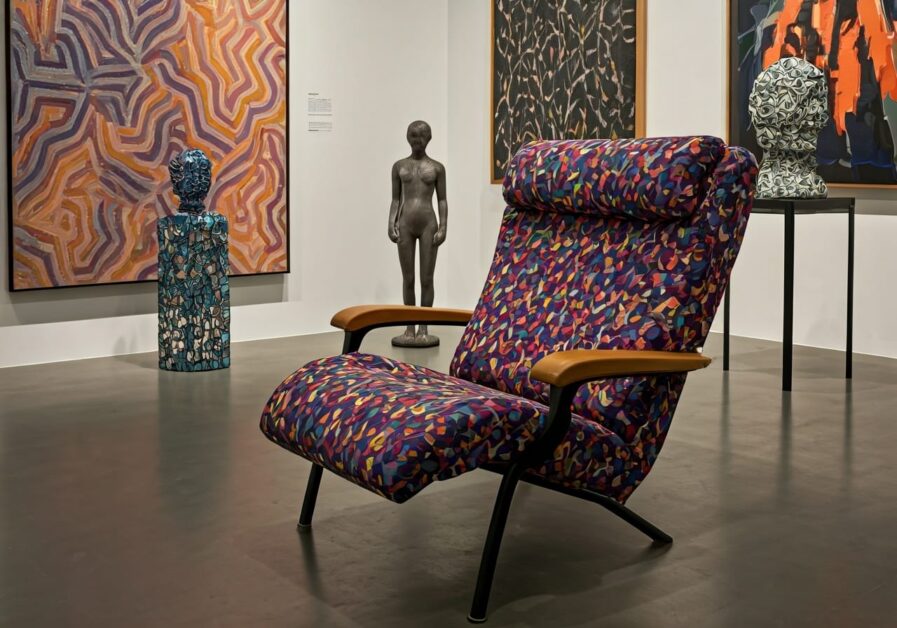 multi-colored modern art living room version of a reclining chair sitting on the floor of an art gallery, along with other pieces of art nearby